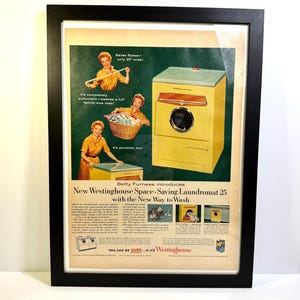 May include: Framed vintage advertisement for the Westinghouse Laundromat 25. The ad features a yellow and teal washing machine, with illustrations of a woman and text that reads "Saves Space - only 25" wide!" and "It's completely automatic - washes a full family-size load!"