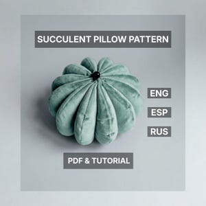 Puede incluir: Un cojín en forma de suculenta de color verde azulado, con un botón negro en el centro. El cojín está hecho de un material suave y aterciopelado. El texto en la imagen dice "SUCCULENT PILLOW PATTERN" y "PDF & TUTORIAL".