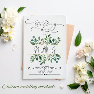 Könnte beinhalten: Ein personalisiertes Hochzeitsnotizbuch mit dem Schriftzug "Wedding day" in eleganter Schrift. Das Cover zeigt ein florales Design mit den Initialen "N G" und dem Datum "23.08.2025". Die Worte "Custom wedding notebook" stehen unten.