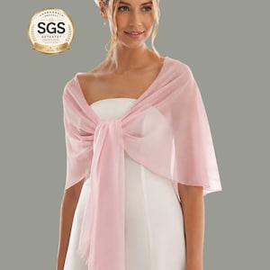 May include: A pale pink chiffon shawl draped over a white dress, tied in a bow. The image shows a woman wearing the shawl, with a neutral background. The shawl adds a touch of elegance to the outfit.