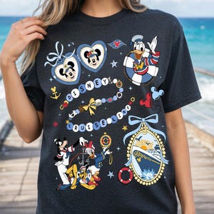 Op de afbeelding: Donkergrijs T-shirt met Disney Cruise Line graphics. Het ontwerp bevat Mickey en Minnie Mouse in hartvormige frames, Donald Duck in een reddingsboei en andere nautische illustraties. De woorden "Disney Cruise Line" worden ook weergegeven.