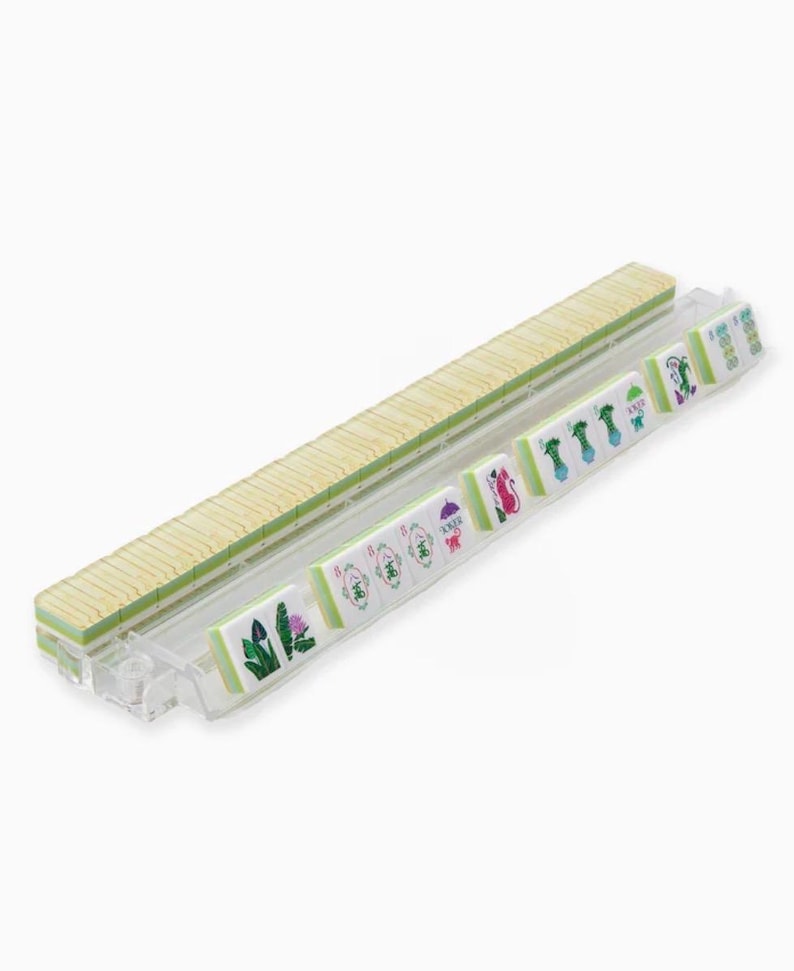 May include: A set of Mahjong tiles, featuring a light wood-colored tile rack and individual tiles with green and white designs. The tiles display various symbols and characters, suggesting a traditional game.