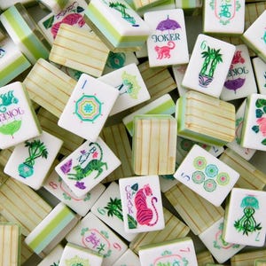 May include: A collection of white and green Mahjong tiles with various symbols and characters. Some tiles feature illustrations of a tiger, monkey, and palm trees. The tiles are arranged in a random pattern.