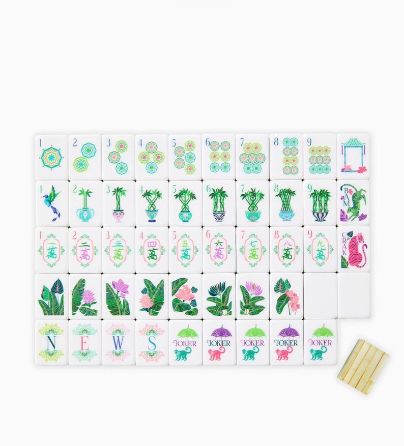 May include: A complete Mahjong set with white tiles featuring colorful illustrations of flowers, plants, and geometric designs. The set includes tiles with numbers, suits, and Jokers, along with a wooden tile holder.