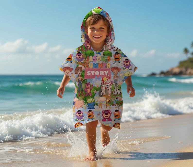 May include: A child wearing a hooded beach towel with a colorful Toy Story design. The towel features various characters from the movie and the text "JASON'S SUMMER STORY". The child is on a sandy beach near the ocean.