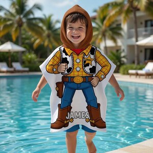 May include: A child wearing a white hooded poncho with a cartoon cowboy design. The poncho features a yellow plaid shirt, a brown vest with black cow spots, blue jeans, and brown boots. The name "JAMES" is printed on the boots.