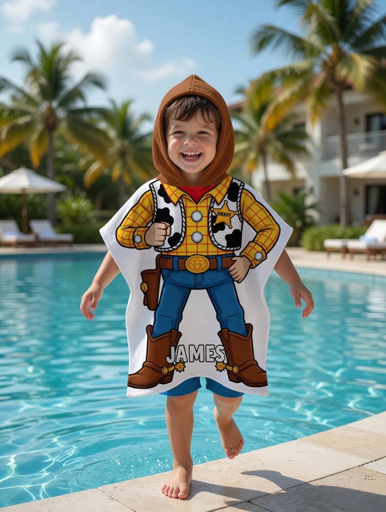May include: A child wearing a white hooded poncho with a cartoon cowboy design. The poncho features a yellow plaid shirt, a brown vest with black cow spots, blue jeans, and brown boots. The name "JAMES" is printed on the boots.