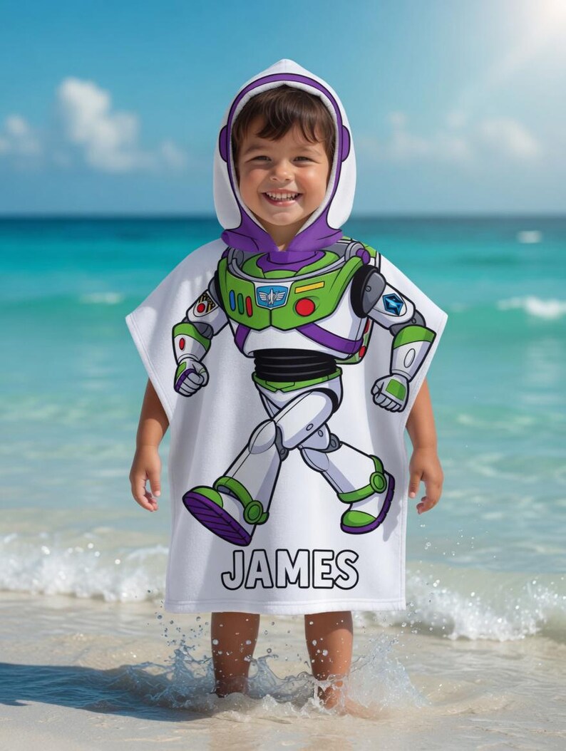 Puede incluir: Toalla de playa blanca con capucha con un dise&ntilde;o de Buzz Lightyear, con detalles verdes, morados y blancos. El nombre "JAMES" est&aacute; impreso en la parte inferior. Un ni&ntilde;o lleva la toalla en la playa.