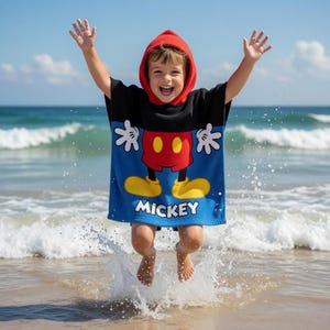 K&ouml;nnte beinhalten: Ein Kind tr&auml;gt einen roten Kapuzenponcho mit Mickey Mouse-Motiv und springt am Strand in die Luft. Der Poncho ist blau mit einem Mickey Mouse-Design, gelben Schuhen, roten Shorts und wei&szlig;en Handschuhen. Das Wort "Mickey" ist unten aufgedruckt.