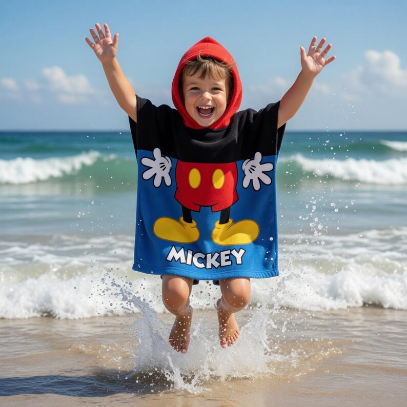 K&ouml;nnte beinhalten: Ein Kind tr&auml;gt einen roten Kapuzenponcho mit Mickey Mouse-Motiv und springt am Strand in die Luft. Der Poncho ist blau mit einem Mickey Mouse-Design, gelben Schuhen, roten Shorts und wei&szlig;en Handschuhen. Das Wort "Mickey" ist unten aufgedruckt.