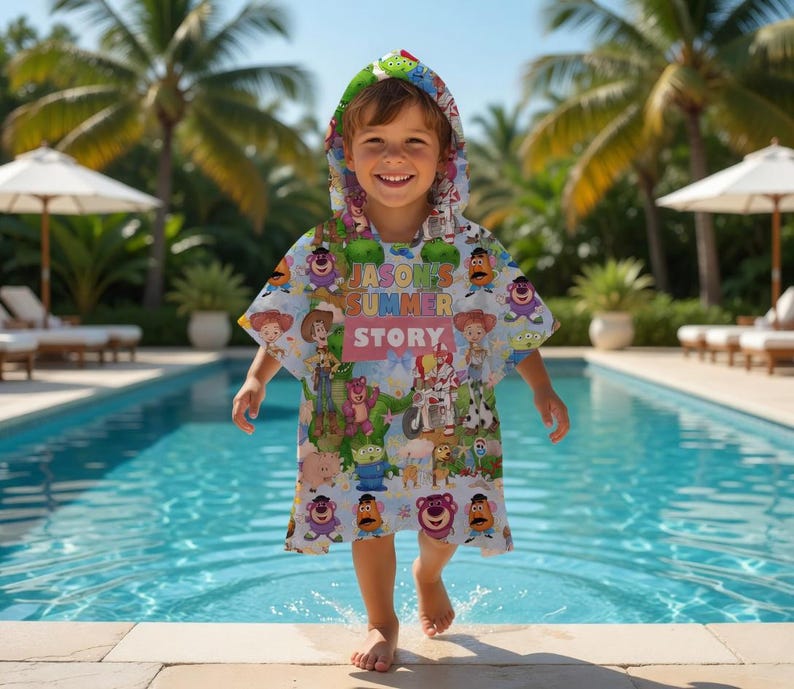 May include: A light blue hooded beach towel featuring various cartoon characters. The towel has the text "JASON'S SUMMER STORY" printed on it. The child is standing near a swimming pool.