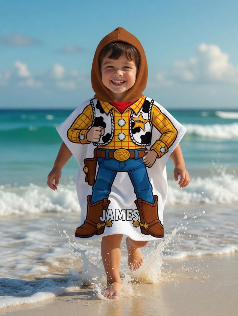 May include: A white hooded beach towel featuring a cartoon cowboy design. The towel has a brown hood and a colorful graphic of a cowboy outfit, including a yellow plaid shirt, blue jeans, and brown boots. The name "JAMES" is printed on the towel.