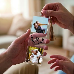 May include: A clear rectangular acrylic bookmark featuring two square photo inserts of a person with a child. The center displays a black graphic of deer antlers surrounding the letter R and the name ROBERT. A gold tassel hangs from the top.