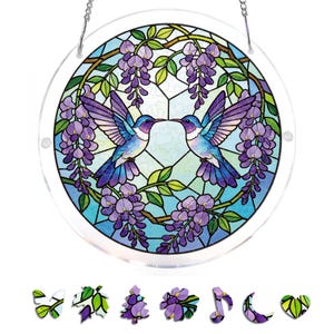 May include: A round, stained-glass window featuring two hummingbirds kissing, surrounded by purple wisteria and green leaves. The window has a clear border and is suspended by a silver chain. Decorative wooden cutouts of flowers and leaves are at the bottom.