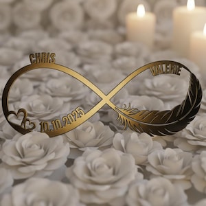 Puede incluir: Un símbolo de infinito dorado con los nombres "CHRIS" y "VALERIE" grabados. Incluye un corazón, una pluma y la fecha "10.10.2025". El objeto está sobre un fondo de rosas de papel blancas y velas encendidas.