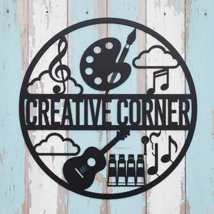 Könnte beinhalten: Schwarze Metall-Wandkunst mit den Worten "CREATIVE CORNER" in einem kreisförmigen Design. Das Design umfasst einen Violinschlüssel, eine Farbpalette, einen Pinsel, Noten, Wolken, eine Gitarre und Farbtuben.