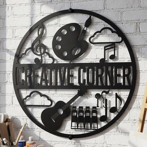 Könnte beinhalten: Ein rundes Wandbild aus schwarzem Metall mit dem Schriftzug CREATIVE CORNER in der Mitte. Das Design zeigt Silhouetten einer Farbpalette mit Pinsel, einer Gitarre, Musiknoten, Wolken und einer Reihe von vier Stühlen innerhalb des Rahmens.