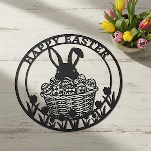 Könnte beinhalten: Schwarze Osterdekoration aus Metall mit einem Hasen und einem Korb mit verzierten Eiern in einem kreisförmigen Rahmen. Die Worte "HAPPY EASTER" sind oben ausgeschnitten. Tulpen in einem Keramiktopf befinden sich im Hintergrund.