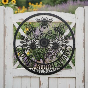 Könnte beinhalten: Ein rundes Wand-Schild aus schwarzem Metall mit einem lasergeschnittenen Design aus drei Bienen über einer Gruppe von Sonnenblumen und Blättern. Der Text "GOLDEN BLOOM APIARY" und "EST. 2023" ist in den unteren Teil des Rahmens integriert.