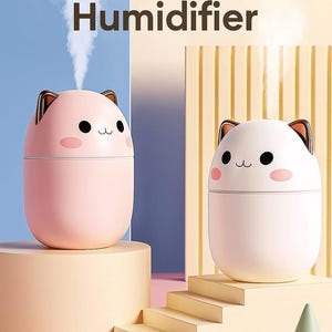 May include: Two cat-shaped humidifiers, one pink and one white, with gold-coloured ear accents. The humidifiers have black eyes and pink cheeks. The text "200ml Humidifier" is at the top. The pink humidifier is on a beige pedestal, and the white one is on a beige pedestal with stairs.