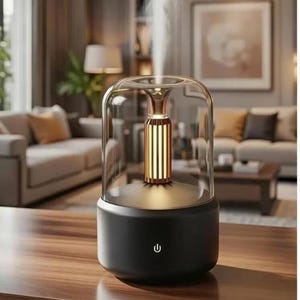 Pu&ograve; includere: Un diffusore di oli essenziali nero e oro con una cupola di vetro. Il diffusore ha un interno cilindrico dorato e un pulsante di accensione. Il vapore bianco sale dall'alto, suggerendo che &egrave; in funzione. Il dispositivo &egrave; posizionato su una superficie di legno.