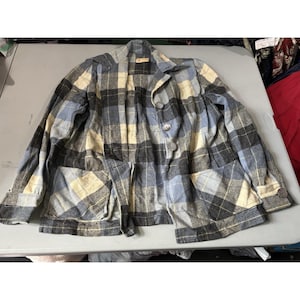 May include: A long-sleeve button-up jacket featuring a plaid pattern in shades of light blue, cream, and dark gray. The jacket includes a collar, two large front patch pockets, and buttons along the front placket and on each of the sleeve cuffs.