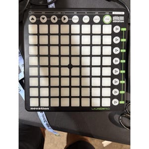 May include: Black Novation Launchpad MIDI controller with a grid of white square buttons. It has function buttons labeled "learn", "view", "page", "session", "user 1", "user 2", "mixer", and "automap". The Ableton logo is visible.