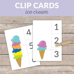 Peut inclure: Cartes à pince blanches avec des illustrations de glaces et les chiffres 1 à 6. Une carte présente un grand cornet de glace avec plusieurs boules de différentes couleurs. Une autre carte montre un plus petit cornet de glace. Une pince à linge en bois est incluse.