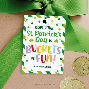 Può includere: Un'etichetta regalo per la festa di San Patrizio con il messaggio "Hope Your St Patrick's Day is BUCKETS of FUN!" in lettere colorate. L'etichetta è bianca con dettagli verdi e un nastro verde. Sono visibili anche monete d'oro con trifogli.