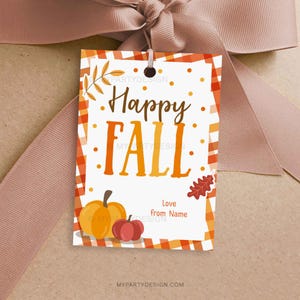 Könnte beinhalten: Ein Geschenkanhänger mit Herbstthema. Der Anhänger zeigt die Worte "Happy Fall" in Orange und Braun, mit einer Kürbis- und einer roten Apfelillustration. Der Anhänger hat einen karierten orange-weißen Rand und ist mit einem braunen Band gebunden.