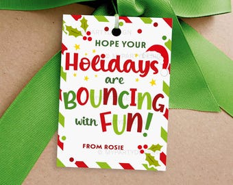 May include: A white gift tag with red and green accents, featuring the text "Hope Your Holidays are Bouncing with FUN!" and a Santa hat illustration. The tag is tied with a green ribbon.