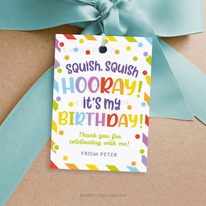 以下が含まれることがあります： 「squish, squish HOORAY! it's my BIRTHDAY!」と「お祝いしてくれてありがとう！」というテキストが入った、カラフルな誕生日のギフトタグ。タグは水色のリボンで結ばれています。