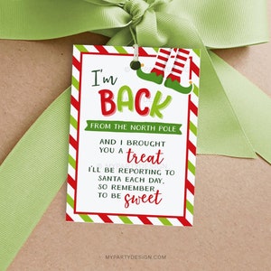 May include: A rectangular gift tag with a red and white striped border and the text "I'm BACK FROM THE NORTH POLE". The tag features elf legs and the words "AND I BROUGHT YOU A treat". A green ribbon is tied around the tag.