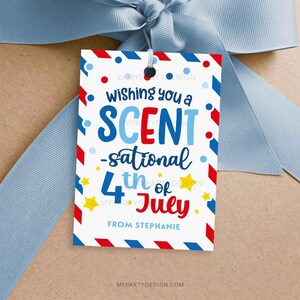 Op de afbeelding: Een witte cadeaulabel met rode, witte en blauwe accenten, met de tekst "Wishing you a Scent-sational 4th of July". De label is vastgebonden met een lichtblauw lint, perfect voor Independence Day.