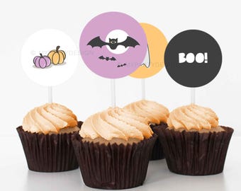 Peut inclure: Quatre cupcakes avec glaçage orange et des décorations sur le thème d'Halloween. Les décorations présentent une citrouille, une chauve-souris et le mot "BOO!" en blanc sur un cercle noir. Les cupcakes sont dans des caissettes marron.