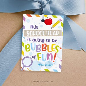 May include: A colorful gift tag with the text "This SCHOOL YEAR is going to be BUBBLES of FUN!" features a red apple, yellow pencil, and a bubble wand. The tag is tied with a light blue ribbon.