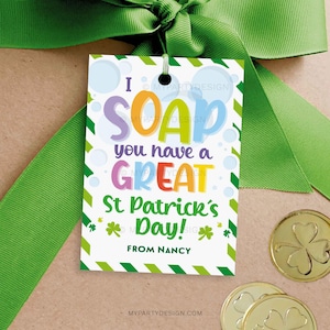 Può includere: Un'etichetta regalo per la festa di San Patrizio con la scritta "I SOAP you have a GREAT St. Patrick's Day!" in lettere colorate. L'etichetta è bianca con dettagli verdi e un nastro verde. Sono visibili anche monete d'oro con trifogli.