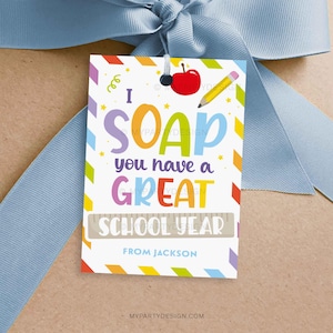 May include: A gift tag with the text "I SOAP you have a GREAT SCHOOL YEAR" in colorful letters. The tag features a red apple and a yellow pencil illustration. The tag is tied with a light blue ribbon.
