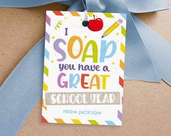 May include: A gift tag with the text "I SOAP you have a GREAT SCHOOL YEAR" in colorful letters. The tag features a red apple and a yellow pencil illustration. The tag is tied with a light blue ribbon.