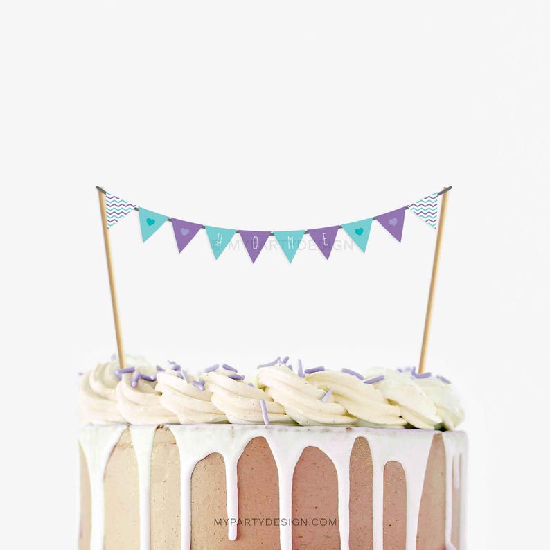 K&ouml;nnte beinhalten: Ein Kuchen mit wei&szlig;em Zuckerguss und einem Banner-Kuchenaufsatz. Das Banner ist t&uuml;rkis und lila mit Herz- und Chevron-Designs. Der Kuchen hat ein braunes und wei&szlig;es Farbschema mit wei&szlig;em Zuckerguss, der an den Seiten heruntertropft. Der Text "#MORMDESIGN" steht auf dem Banner.