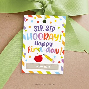 May include: A white gift tag with colorful text that reads "SIP, SIP HOORAY! Happy first day!" The tag features a red apple, a yellow pencil, and a ruler graphic. The tag is tied with a green ribbon.