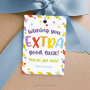 Puede incluir: Una etiqueta de regalo blanca con confeti colorido y el texto "Wishing you EXTRA good luck! You've got this! From Coach." La etiqueta está atada con una cinta azul claro.