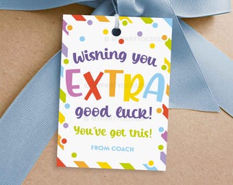 May include: A white gift tag with colorful confetti and the text "Wishing you EXTRA good luck! You've got this! From Coach." The tag is tied with a light blue ribbon.
