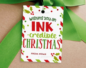 May include: A white gift tag with red and green accents, featuring the text "wishing you an INK-credible CHRISTMAS" in a festive font. The tag is tied with a green ribbon, perfect for holiday gifts.