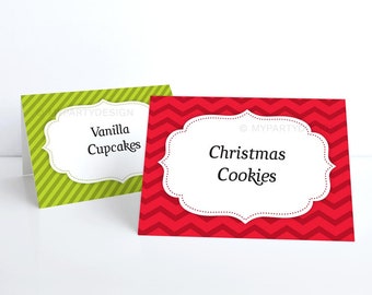 May include: Two decorative table signs. One is green with diagonal stripes and the text "Vanilla Cupcakes". The other is red with a chevron pattern and the text "Christmas Cookies". Both signs have a white, scalloped border.