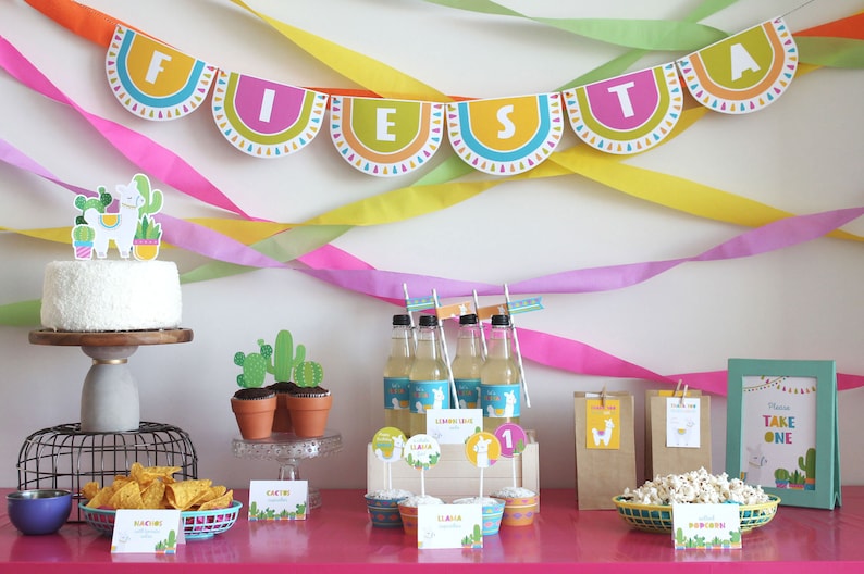 Pu&ograve; includere: Una tavola da festa a tema fiesta colorata con una torta bianca decorata con un lama e cactus, cupcake con topper a forma di lama, bottiglie di limonata, una ciotola di popcorn e un cartello che dice "Prendi pure uno".