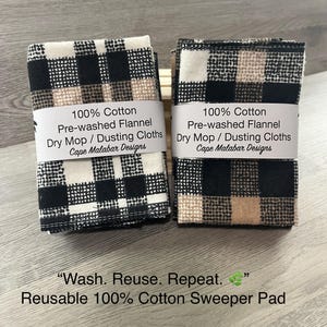 May include: Two stacks of folded 100% cotton pre-washed flannel dry mop and dusting cloths featuring a black, white, and tan buffalo check pattern. Each stack is wrapped in a white paper band labeled 100% Cotton Pre-washed Flannel Dry Mop / Dusting Cloths Cape Malabar Designs.