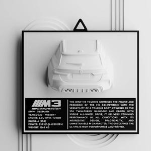 May include: A white 3D model of a BMW M3 Touring car, mounted on a black frame. The image includes text detailing the car's specifications, including the engine, power, and weight. The text also describes the car's performance and design.