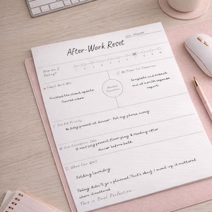 May include: A white "After-Work Reset" notepad with handwritten notes, a pink mousepad, a white keyboard, and a coffee cup. The notepad includes sections for feelings, work wins, and future focus. A pen and notepad are also visible.