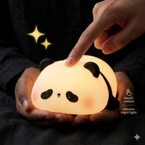 Puede incluir: Una suave y brillante luz nocturna con forma de panda. El panda tiene orejas, ojos y una raya negros, con mejillas rosadas. La luz se sostiene en manos ahuecadas, con un dedo tocando la superficie del panda. El texto dice "touch control" y "silicone night light."